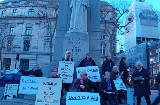 Vigil - women hold posters saying don't cut aid, tax wealth