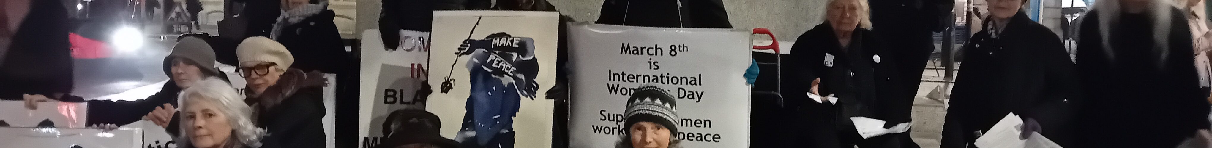 Women gather around statue with placards for International Women's Day