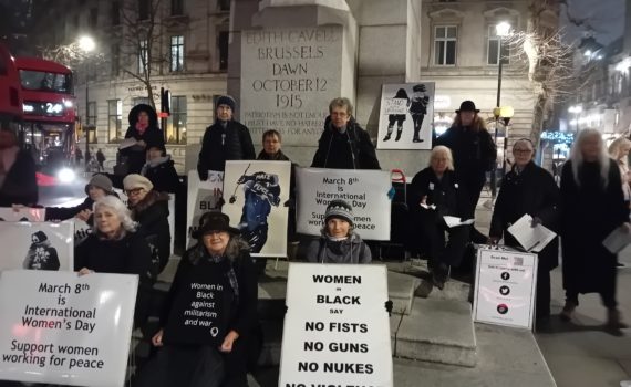 Women gather around statue with placards for International Women's Day